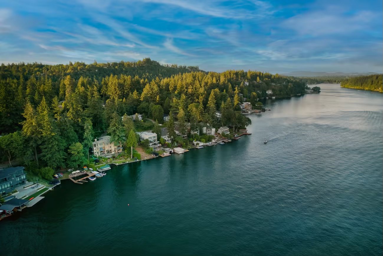 An aerial view of Lake Oswego, showing a serene lake surrounded by dense green forests and waterfront homes with docks