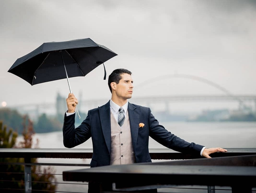 A client of The House Of Rose elegantly dressed in a bespoke three-piece suit holding an umbrella in Portland, Oregon